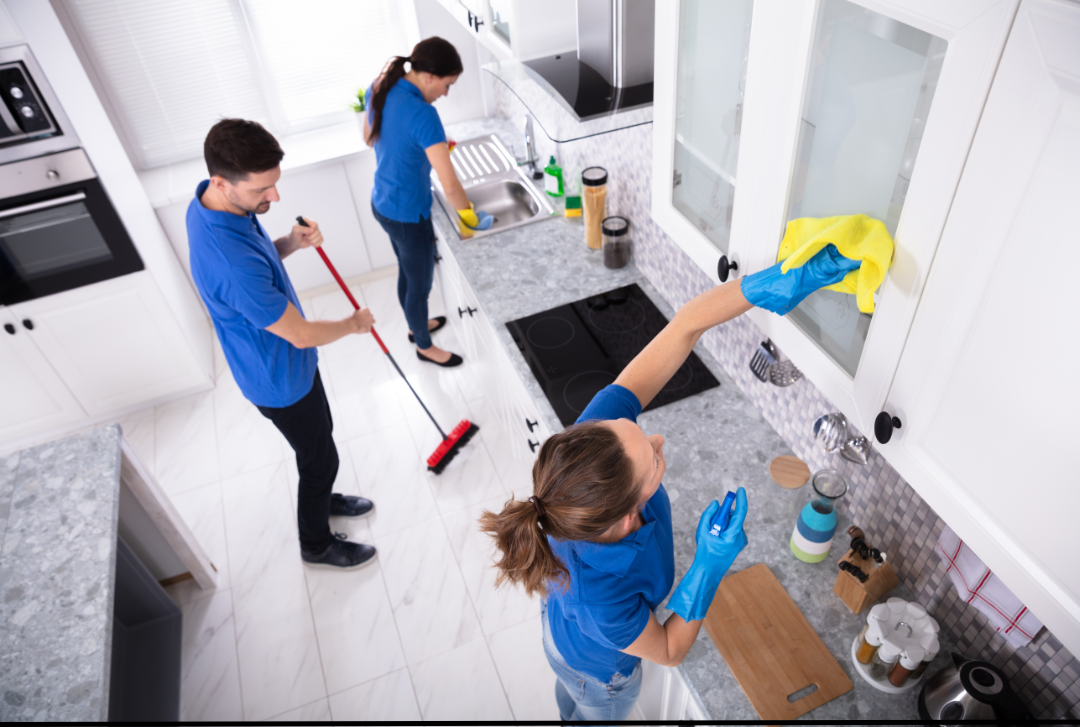 Three individuals work as a team to sweep and scrub a kitchen