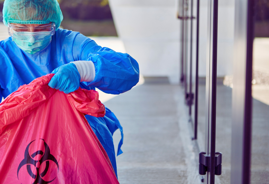 a person wearing full personal protection equipment places an object in a red biohazard bag